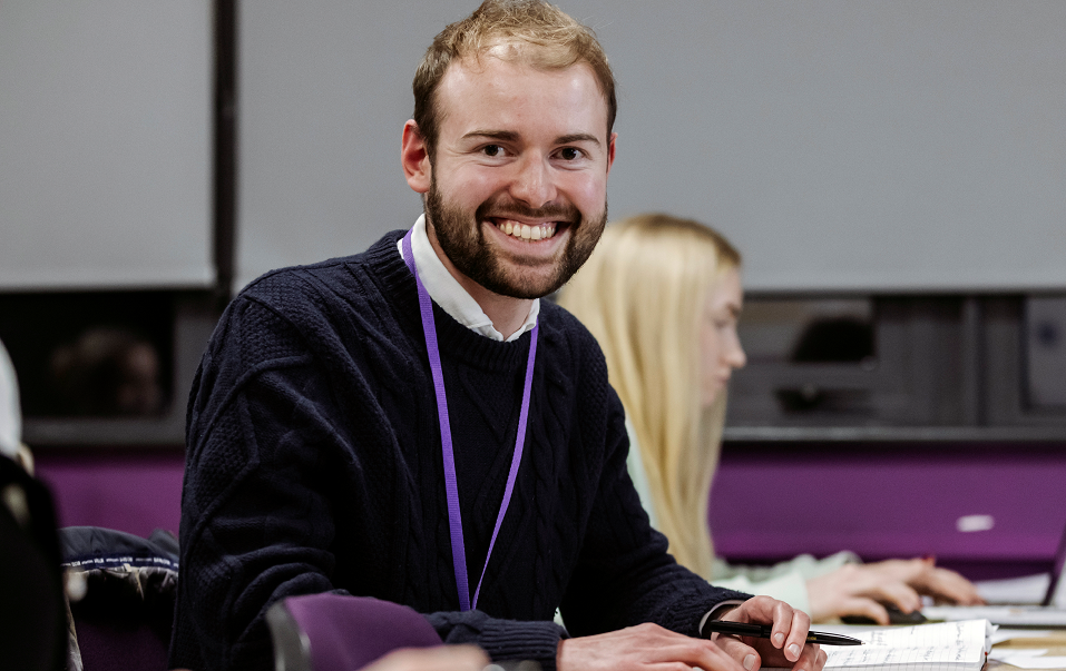 Male Student Smiling Sat At Desk